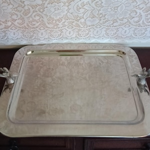 May include: A square silver-toned metal serving tray with a polished reflective surface and rounded corners. The tray features two decorative handles shaped like deer heads with antlers, positioned on the left and right sides of the tray.