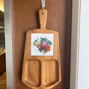 May include: A wooden serving tray with two divided sections and a tile insert featuring a floral design with plums and berries. The tray is hanging on a hook.