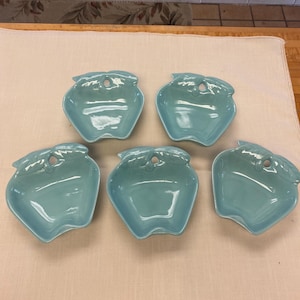 May include: Set of five light blue ceramic apple-shaped bowls. The bowls have a small hole in the top and a leaf design around the rim.