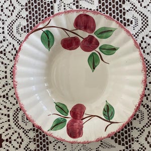 May include: A white ceramic bowl with a pink rim and a hand-painted design of red apples and green leaves.