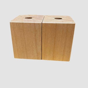 May include: Two wooden blocks with a hole in the top, side by side. The blocks are a light brown color and have a smooth surface.