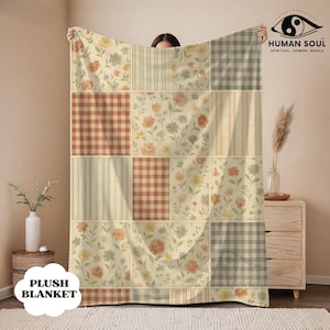 Puede incluir: Una manta de felpa con diseño de patchwork. La manta presenta cuadrados con estampados florales, a rayas y de cuadros en tonos crema, naranja y azul. Las palabras "PLUSH BLANKET" están impresas en la parte inferior izquierda.
