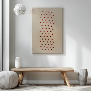 May include: A rectangular canvas art piece with a beige background and a vertical pattern of red dots. The artwork hangs on a white wall above a wooden bench. A white vase and a gray ottoman are in the foreground.