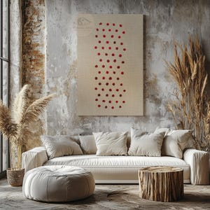 May include: A beige canvas wall art piece with a pattern of red dots. The artwork hangs above a white sofa with several pillows. A round ottoman and a wooden stump table are in front of the sofa.
