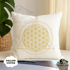 May include: Off-white pillow cover with a gold geometric design featuring a flower of life pattern. The pillow has a square shape and the words "PILLOW COVER" are printed on the bottom left.