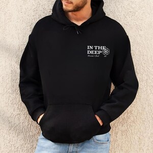May include: Black hooded sweatshirt with a front pocket and drawstring. The text "IN THE DEEP" is printed on the upper left chest, along with a geometric design and the words "Human Soul".