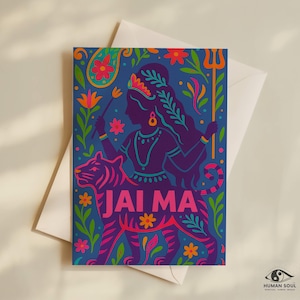 May include: A greeting card with a blue background featuring a purple illustration of a woman riding a tiger, with the words "JAI MA" in pink. The card is decorated with floral and paisley designs and is accompanied by a white envelope.
