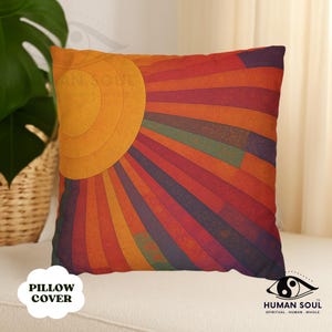 May include: Square pillow cover with a vibrant sunburst design in shades of orange, red, and purple. The pillow features a large, circular sun shape and radiating lines. The words "PILLOW COVER" are printed on the bottom left.