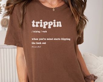 Peut inclure: T-shirt marron avec un graphisme blanc qui dit "trippin" et définit le mot comme "quand votre esprit commence à se retourner".