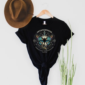 May include: Black t-shirt with a graphic of a butterfly inside a geometric design. The text "Metamorphosis" and "Embrace Your Transformation" is printed on the shirt.