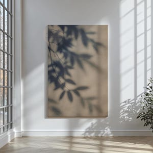 May include: A large canvas print featuring a neutral beige background with a dark gray shadow of leaves and branches. The artwork is displayed on a white wall in a well-lit room with a wooden floor.