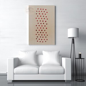 May include: A rectangular canvas art piece with a beige background features a vertical pattern of red dots. The artwork hangs above a white sofa with two pillows. A black floor lamp and side table with a candle are also visible.