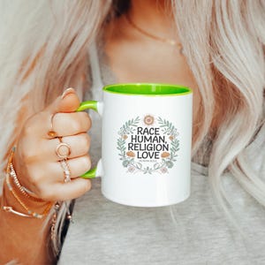 May include: White ceramic mug with a green interior and handle. The mug features the text "RACE, HUMAN, RELIGION, LOVE" surrounded by a floral wreath. The words "HUMAN SOUL" are printed below the text.