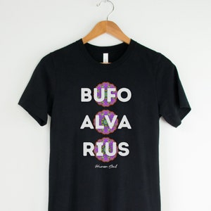 May include: Black t-shirt with white text that reads "BUFO ALVARIUS" with a purple and green mandala design below each word. The text "Human Soul" is printed in smaller white text below the mandala designs.