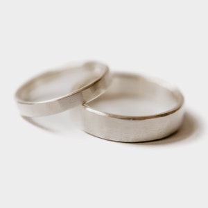 Handmade Silver Wedding Band Set. This photo shows two forged sterling silver rings. (Mens band horizontal Womens band horizontal  on top of mens ring with white background)