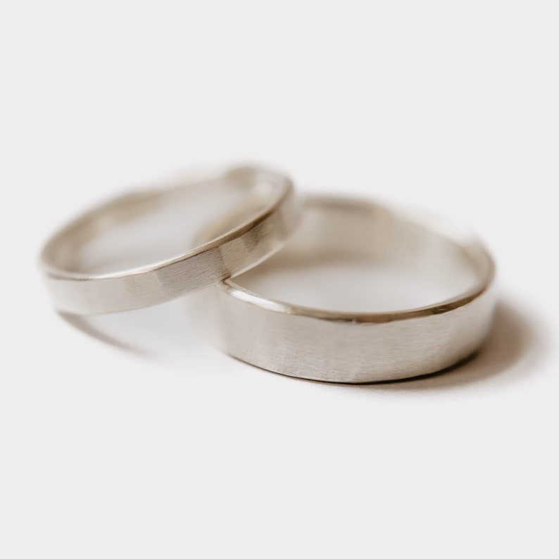 Handmade Silver Wedding Band Set. This photo shows two forged sterling silver rings. (Mens band horizontal Womens band horizontal  on top of mens ring with white background)