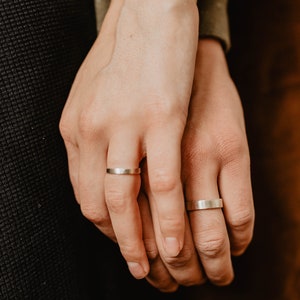 Handmade Silver Wedding Band Set. This photo shows two forged sterling silver rings. (Rings are shown on man's and woman's fingers)