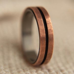 May include: A copper ring with a black inlay and a brushed finish. The ring has two parallel lines running around the band.