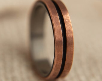 May include: A copper ring with a black inlay and a brushed finish. The ring has two parallel lines running around the band.