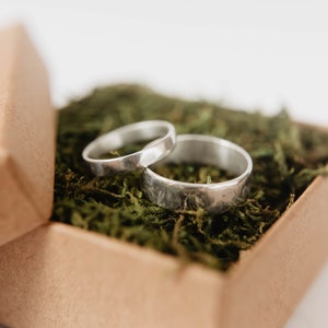 Handmade Silver Wedding Band Set. This photo shows two forged sterling silver rings. (Mens band horizontal Womens band horizontal  on top of mens ring in ring box with moss)