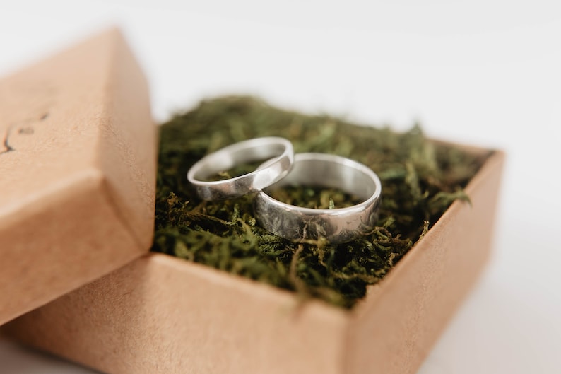 Handmade Silver Wedding Band Set. This photo shows two forged sterling silver rings. (Mens band horizontal Womens band horizontal  on top of mens ring in ring box with moss)