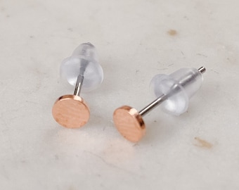 Puede incluir: Un par de pendientes de botón de oro rosa con un diseño circular. Los pendientes son pequeños y delicados.