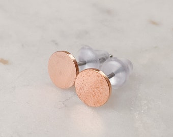Puede incluir: Un par de pendientes de botón de oro rosa con un diseño circular. Los pendientes están sobre una superficie de mármol blanco.