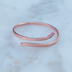 Peut inclure: Une bague simple et délicate en or rose avec une finition martelée. La bague est ouverte et s'enroule autour du doigt.
