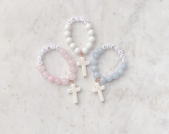May include: Three beaded bracelets with cross charms. The bracelets are made with white, pink, and blue beads. The beads are lettered with the words "Faith", "Blessed", and "Blessed".