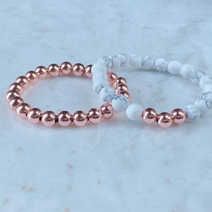May include: Two bracelets, one with rose gold beads and one with white marble beads.