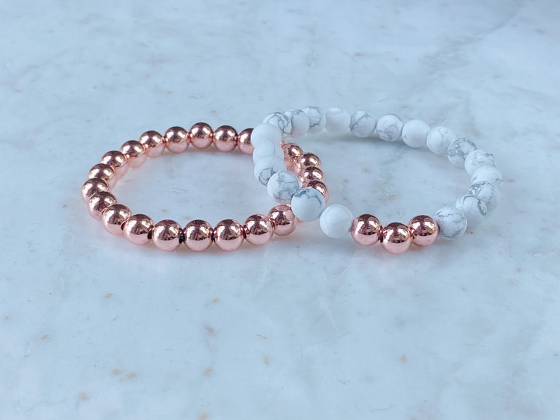 May include: Two bracelets, one with rose gold beads and one with white marble beads.