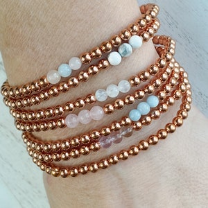 May include: A set of seven bracelets featuring copper beads and a variety of semi-precious stones, including rose quartz, aquamarine, and white stones.