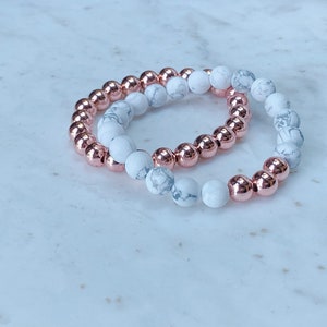 May include: Two bracelets, one with white and gray marble beads and the other with rose gold beads.