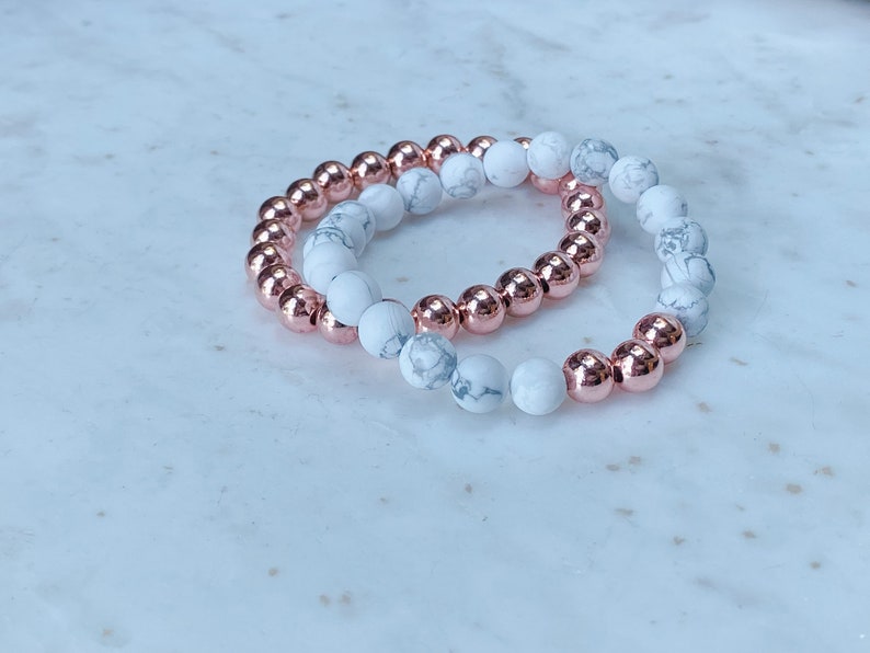 May include: Two bracelets, one with white and gray marble beads and the other with rose gold beads.