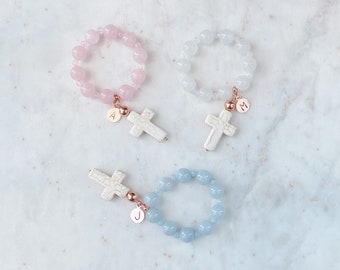 May include: Three bracelets with white cross charms and initial charms. The bracelets are made with pink, white, and blue beads.