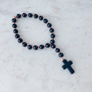 May include: A black beaded rosary with a black cross pendant. The beads are separated by small rose gold accents.