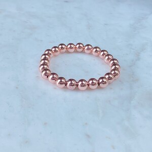 May include: A rose gold beaded bracelet with a simple design. The bracelet is made of small, round beads that are strung together on a stretchy cord.