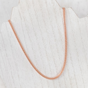 May include: A rose gold chain necklace on a white display stand.