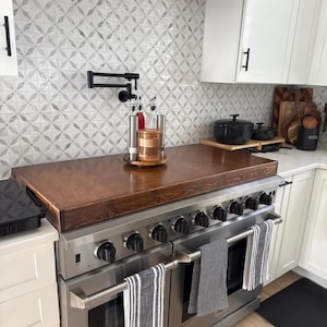 May include: A stainless steel range with six burners and two ovens. The range has a wooden countertop and a black faucet mounted on the wall above it. There are three glass bottles and a wooden container on the countertop.