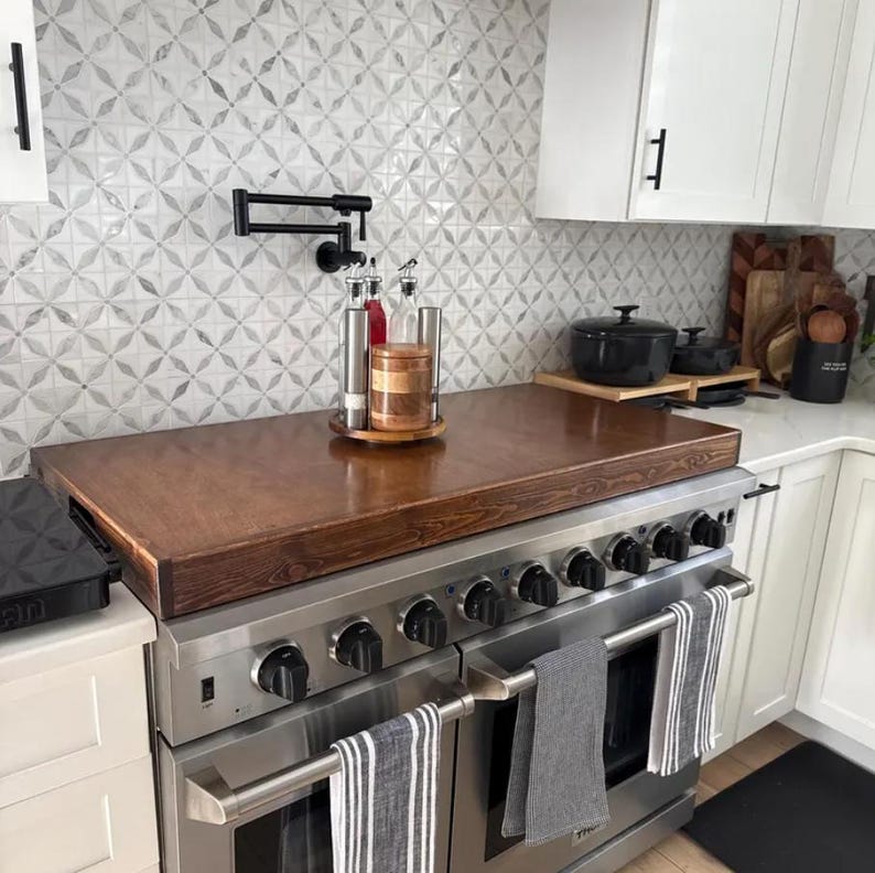 May include: A stainless steel range with six burners and two ovens. The range has a wooden countertop and a black faucet mounted on the wall above it. There are three glass bottles and a wooden container on the countertop.
