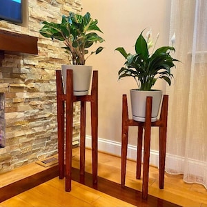 May include: Two wooden plant stands with two potted plants. The stands are dark brown wood and the pots are white.