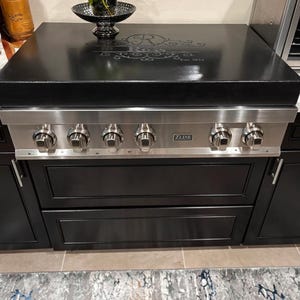 May include: A black and stainless steel gas stove with four burners and a black countertop. The countertop has a decorative design with the text "Est. 1912". The stove has a silver ZLINE logo.
