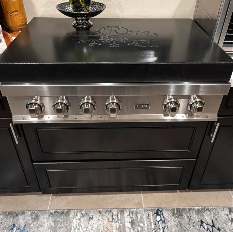 May include: A black and stainless steel gas stove with four burners and a black countertop. The countertop has a decorative design with the text "Est. 1912". The stove has a silver ZLINE logo.