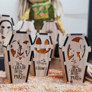 May include: Set of five wooden Halloween-themed candle holders shaped like coffins. Two coffins feature a couple embracing with the text "Till Death Do Us Part", one coffin has a jack-o-lantern face with the text "Happy Halloween", and two coffins feature a couple embracing with the text "Till Death Do Us Part".