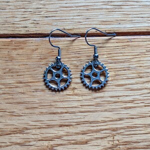Peut inclure: Une paire de boucles d'oreilles argentées avec un motif d'engrenage. Les boucles d'oreilles sont sur une surface en bois.