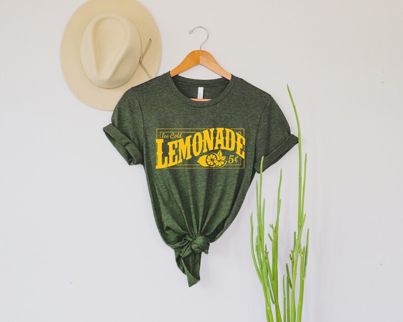 May include: A dark green t-shirt with a yellow graphic that says "Ice Cold Lemonade 5&cent;" with a lemon slice illustration.