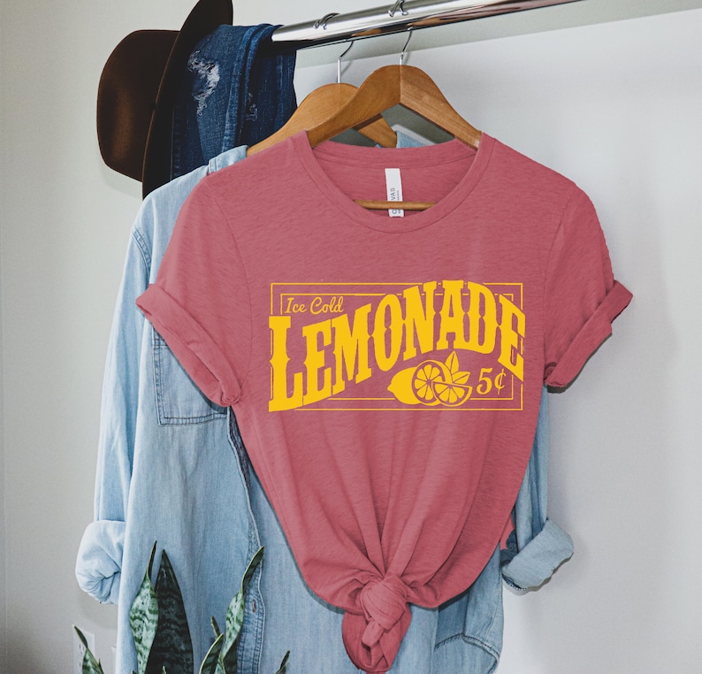 May include: A pink t-shirt with a yellow graphic that says "Ice Cold Lemonade 5&cent;" with a lemon illustration.