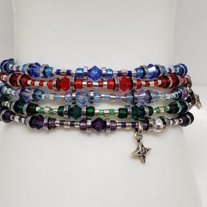 May include: A multi-strand bracelet featuring five rows of beads in blue, red, light blue, green, and purple. Each row includes faceted crystal beads, small round beads, and silver-toned spacers. A four-pointed star charm hangs from the bottom row.
