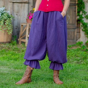 May include: Deep purple loose-fitting trousers featuring a textured fabric, side pockets, and ruffled hems at the ankles. The pants have a gathered, voluminous silhouette and are paired with brown lace-up boots and a red top.