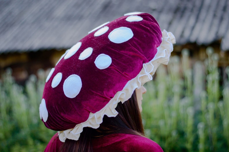 May include: A red velvet mushroom hat with white polka dots and a white lace trim.